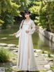 A woman in a white dress standing next to a pond.