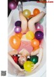 A woman laying in a bathtub filled with colorful balloons.