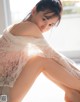 A woman in a white lace top sitting on a window sill.