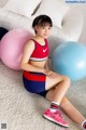 A young woman sitting on the floor next to two exercise balls.